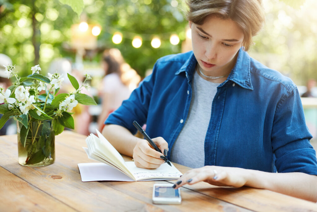 woman taking notes using smartphone outdoor portrait young woman writing her notebook