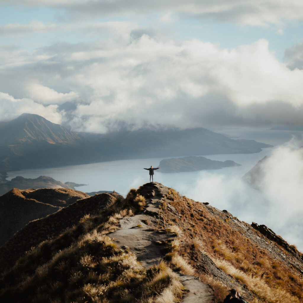 man with hands wide open standing top mountain enjoying incredible view lake