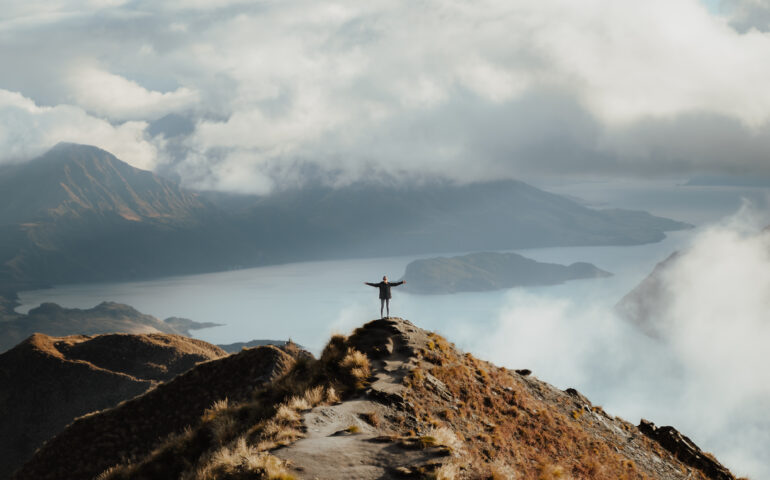 man with hands wide open standing top mountain enjoying incredible view lake